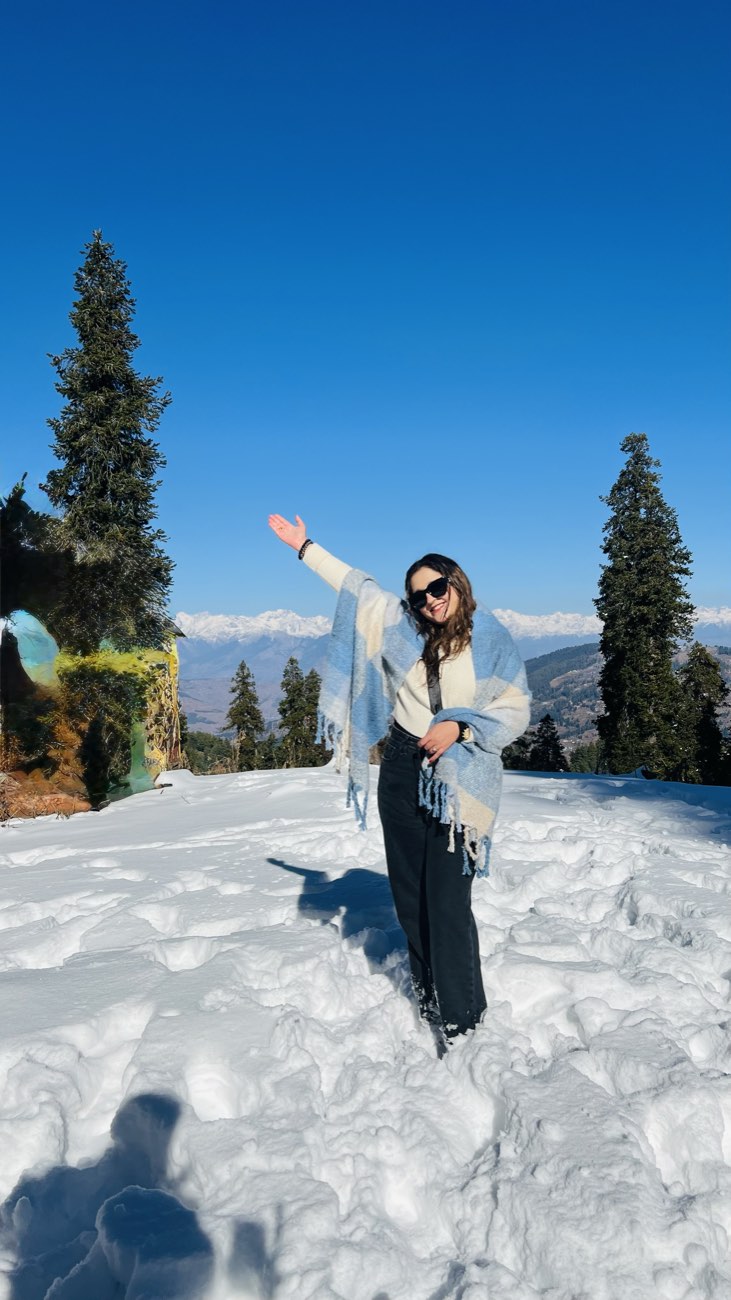 Kashish standing in fresh snow on a mountain ridge, arms out